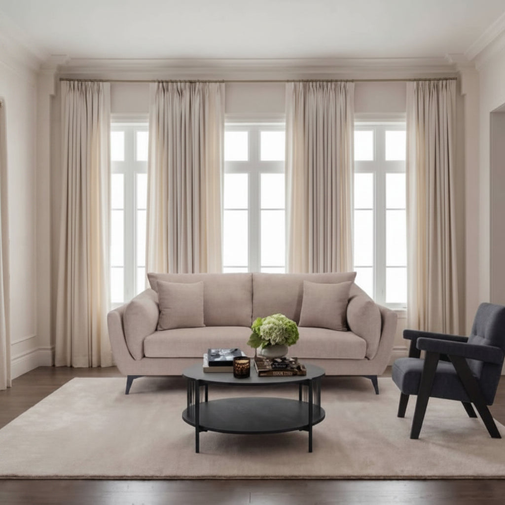 Living room with beige sofa, coffee table, and armchair in front of large windows with curtains.