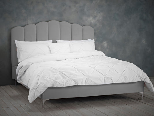 Grey upholstered bed with white bedding  and a panelled style headboard